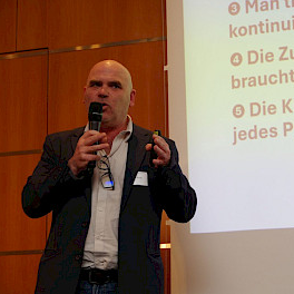 Beim Vortrag zum Thema KI auf dem Kongress der Sozialwirtschaft in Berlin: Mikrofon in der Hand, im Hintergrund eine Präsentationsfolie.